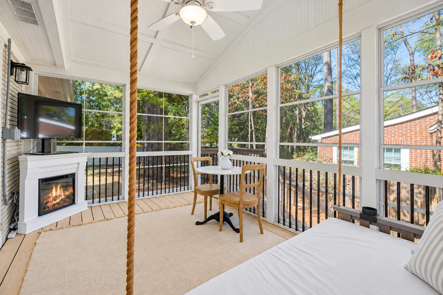 Bright enclosed patio room with large windows, a small table, fireplace, television, and ceiling fan.