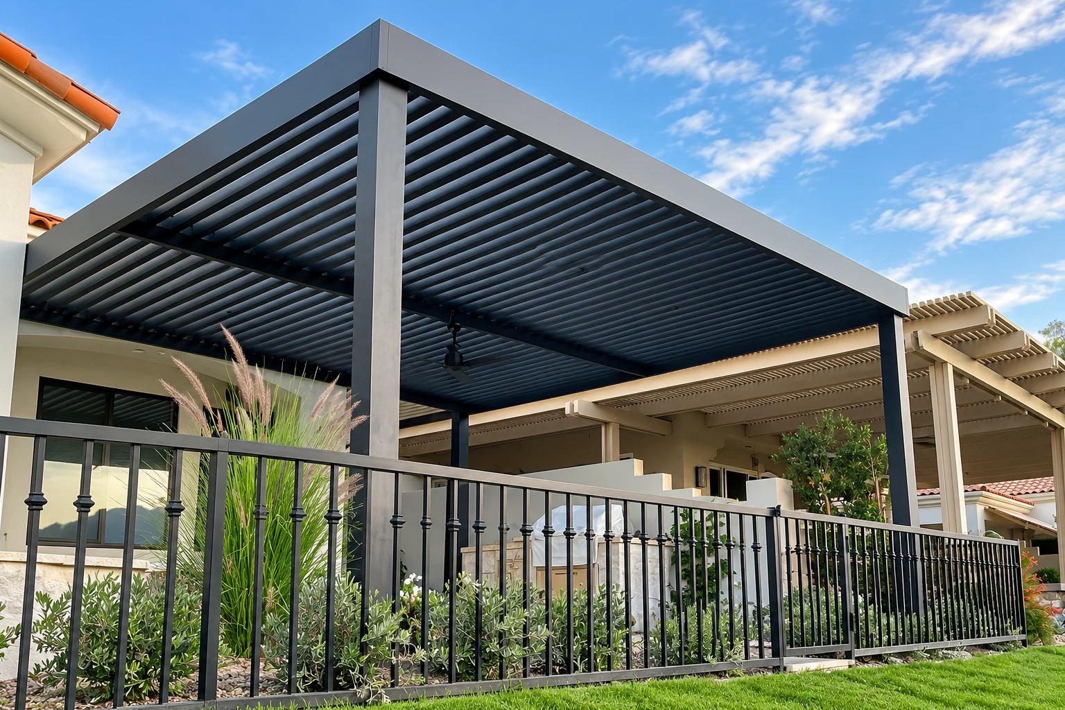Modern dark metal patio cover with slatted roof over a fenced outdoor seating area.