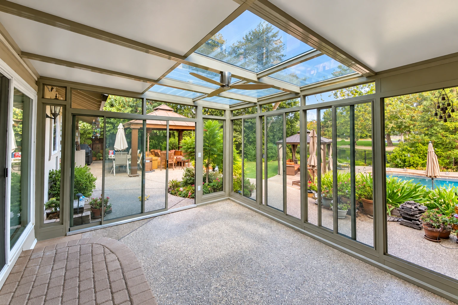 Enclosed patio room with glass walls, a skylight ceiling, and views of a landscaped patio and pool.