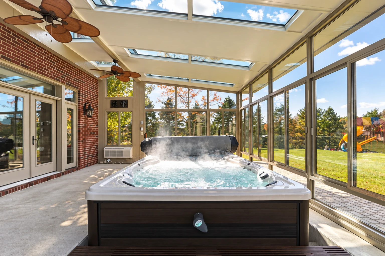 Sunroom addition with a bubbling hot tub, skylights, ceiling fans, and floor-to-ceiling windows overlooking a lawn.